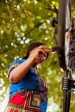 Sağlıklı, zinde bir zenci kadın dışarıda bozuk bir bisiklet kolu ve pedalını tamir etmeye çalışıyor. Bisikletin düzgün çalışmasını sağlayan Afro-Amerikan genç bir kadınla açık hava bakım aktivitesi..