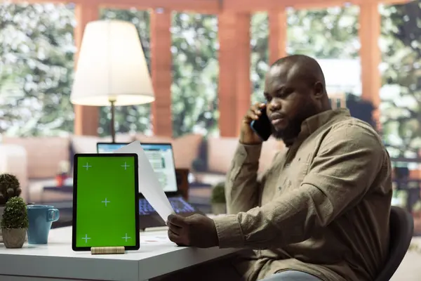 stock image Businessman talks on phone call with investors next to isolated copy space screen, creating data analytics reports from his home office. Entrepreneur negotiates with shareholders remotely.