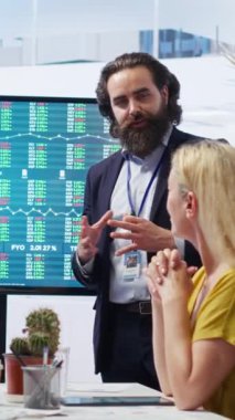 Ofisteki dikey video komisyoncusu müşterilerine finansal tavsiyelerde bulunuyor. Büyük ekrandaki borsa dalgalanmalarına bakıyor. Piyasa büyümesini anneyle analiz eden mali danışman ve