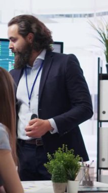 Dikey video finans danışmanı, büyük ekran kullanarak müşterilere pazar analizleri sunarak, veriye dayalı karar verme sürecini vurguluyor. Borsa göstergeleri hakkında istatistiksel çizelgeler gösteren broker