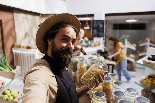 Stock image Zero waste shop entrepreneur using selfie camera on smartphone to promote environmentally conscious vegan products online. Ecofriendly supermarket owner making social media content for followers