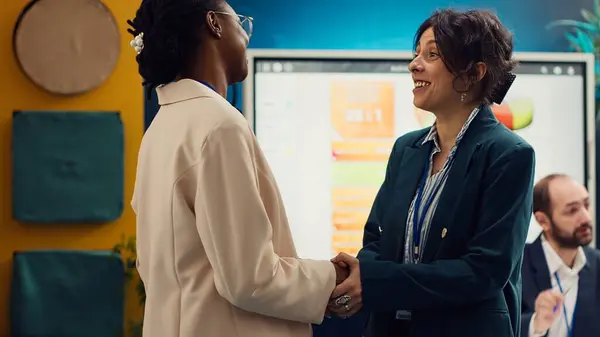 stock image Project manager sharing insight about a new strategy with the new employee, shaking hands and welcoming her to the team in conference room. Coworkers in a new hire introductions meeting. Camera A.