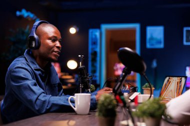 Afrikalı Amerikalı bir adam kulaklık takıp mikrofona konuşurken online tartışmaları yönetiyor. Erkek içerik yaratıcısı podcast ekipmanlarıyla canlı bir talk show yayınlıyor.