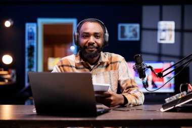 Siyah erkek blogcu elinde bir defter, kameraya bakıyor ve çevrimiçi izleyicileriyle birçok konuyu tartışıyor. Afrikalı Amerikalı etkileyici bir kitaptan özet okuyarak video içeriği oluşturur.