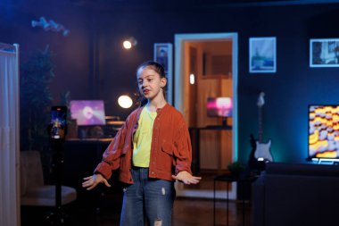 Sosyal medya için tripod dengeleyicisiyle cep telefonuyla video çekerken dans eden ve şarkı söyleyen bir kız. Gülümseyen çocuk, cep telefonuyla kaydedilen profesyonel koreografiyle hayranlarını eğlendiriyor