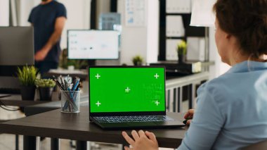Ofis masasında dizüstü bilgisayarında yeşil ekran ile çalışan yönetici, model krom anahtar görüntüsünü ve izole edilmiş telif alanı şablonunu analiz ediyor. İş yerinde kişisel bilgisayar kullanan bir kadın.
