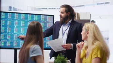 Şirket finans departmanındaki takım lideri yatırım varlıklarının toplandığı büyük ekranda hisse senedi portföyünü gösteriyor. Büyük ekranda hisse senedi talebi artışı gösteren işadamı, kamera B