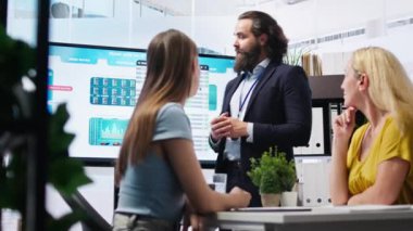 Finansal danışman, geniş ekran kullanarak müşterilere piyasa analizlerini sunuyor, portföy inşa etmek için en iyi uygulamaları keşfediyor. Broker ajanı anne ve kızına borsa çizelgeleri gösteriyor, kamera A