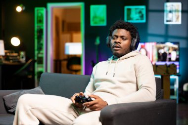 BIPOC oyuncusu evde, kanepede oturuyor boş zamanlarında dizüstü bilgisayarında oyunların keyfini çıkarıyor. Adam dairede kanepede oturuyor, bilgisayar oyunu oynuyor, işten sonra dinleniyor.