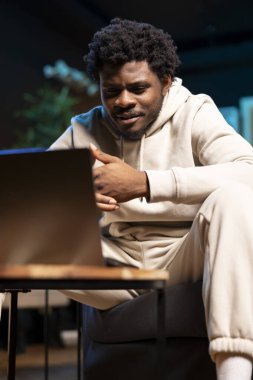 BIPOC uzaktan kumandalı çalışanı gece geç saatlerde evinde, dizüstü bilgisayarın önünde oturuyor ve çok düşünüyor. Son teslim tarihinden önce işi bitirmeye çalışan adam, çözümler bulmaya çalışıyor