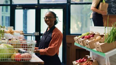 Yerel süpermarketteki Afrikalı Amerikalı kadın rafları yeni toplanmış ürünlerle dolduruyor. Mahalledeki küçük işletme sahibi. Depo görevlisi yeniden kullanılabilir konteynırlarda kiler düzenlemesi yapıyor.