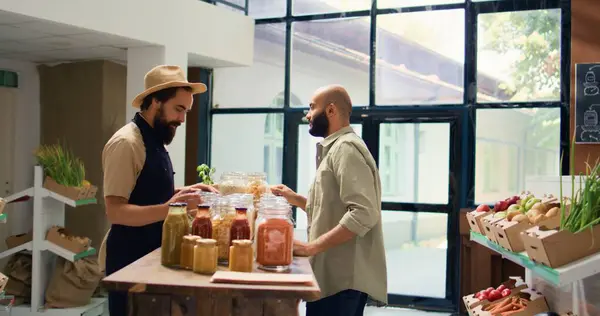 stock image Shop owner shows pasta types to client, opening reusable containers filled with bulk items in natural bio grocery store. Vendor recommending organic additives free food goods.