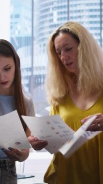 Finansal danışman tarafından piyasa eğilimlerini analiz eden ve gelirlerini optimize etmek için bilgilendirilmiş tavsiyelerde bulunan dikey video istemcileri istatistiksel tablolara bakıyorlar. Yatırım planı okuyan kadınlar