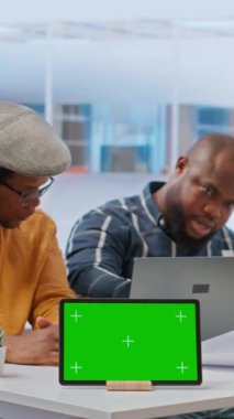 Dikey Video İşletmecisi tablette kroma anahtarının yanındaki emlakçılarla tartışıyor, ofis taşınma planlarına bakmadan önce kira sözleşmesi şartlarını görüşmek için buluşuyor.
