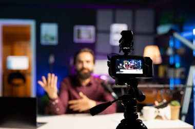 Vlog kanalı girişinde bulanık arka planda medya yıldızının kullandığı profesyonel kayıt ekipmanlarına odaklan. Hayranlarını selamlarken kendini kaydetmek için kullanılan kamerayı kapat