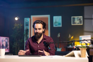 Stüdyoda sponsorluk videosundan dizüstü bilgisayarı destekleyen profesyonel mikrofonla konuşan bir adam. İçerik oluşturucu, yüksek teknoloji mikrofonuyla kayıt yaparak, dizüstü bilgisayarın tanıtımını yapıyor.
