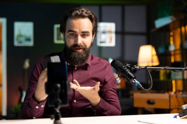 Teknoloji gurusu V mount bataryasını sunuyor, cep telefonunu tripoda ve profesyonel mikrofonda kullanarak teknoloji incelemesi yapıyor. Kafkas vlog kaydedicisi şarj aygıtı özelliklerini gösteriyor, telefonla kaydediliyor