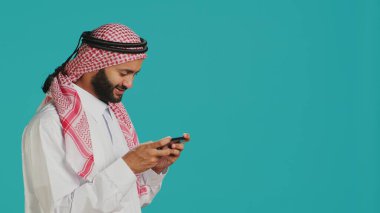 Arapça konuşan, akıllı telefondan oyun oynayan, gergin ifadeli, başörtüsü ve başörtüsü takan biri. Stüdyodaki telefon uygulamasında online oyun deneyiminin tadını çıkaran Müslüman bir oyuncu.