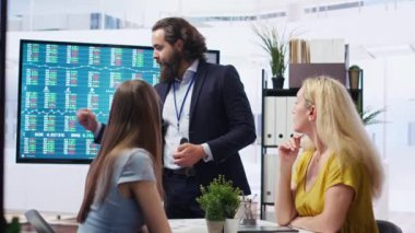 Finansal danışman müşterilerine pazar analizlerini geniş ekran kullanarak sunuyor ve veriye dayalı karar verme sürecini vurguluyor. Borsa göstergeleri hakkında istatistiksel çizelgeler gösteren broker, kamera B