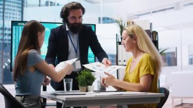 Finansal danışman müşterilere büyük ekranda veri grafikleri gösteriyor, tahmin yapmak için piyasa eğilimlerini analiz ediyor. Anne ve Z kızı, A kamerasının yaptığı yatırım planlarını kontrol ediyor.