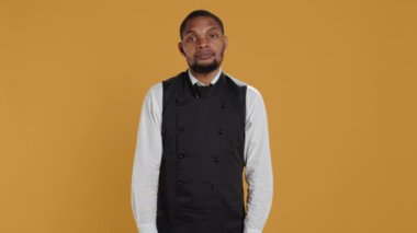 Profesyonel garson hiçbir şey bilmiyor ve emin değil, omuz silkiyor ve stüdyoda bilmediğimi söylüyor. Önlüklü şaşkın uşak bir şey hakkında kararsız ve kuşkulu hissediyor. Kamera B.