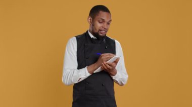 Önlüklü yetenekli garson müşterilerden yemek siparişlerini not defterine alır müşteri memnuniyeti için önemli bilgiler yazar. Hizmet odaklı sektörde çalışan kahya. Kamera B.