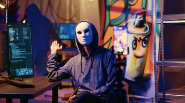 Gizli yeraltı üssünde fidye videosu çeken maskeli hackerlar, ödeme talepleri karşılanmazsa çalınan verileri halka açıklamakla tehdit ediyorlar. Düzenbaz programcılar şantaj görüntülerini kaydetmek için telefon kullanıyorlar.