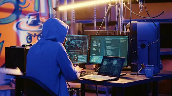 stock image Hacker in abandoned warehouse with graffiti walls writing code that spoofs his location, tricking cops. Rogue developer running script on many devices pinging wrong location to cybercriminal police