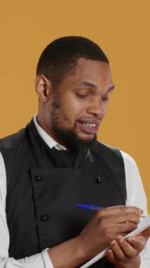 Önlüklü Dikey Video Becerikli Garson müşterilerden yemek siparişlerini bir deftere alır ve müşteri memnuniyeti için önemli bilgiler yazar. Hizmet sektöründe çalışan kahya.