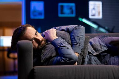 Adam yastığa uzanmış televizyon seyrediyor, kalbi kasvetli film senaryosuyla kırılıyor. Üzgün izleyiciler, RGB 'nin aydınlatılmış dairesinde, iç karartıcı televizyon şovu sahnesinden dolayı üzgün bir şekilde kanepede uzandılar.