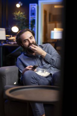 Komik komedi filmi izlerken koltukta oturup gülen, patlamış mısır yiyen çok mutlu bir adam. Apartman dairesinde atıştırmalık yiyen ve film sahnesinde komik bir şakayla eğlenen neşeli bir insan.