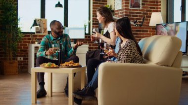Çok ırklı bir arkadaş grubu sıcak bir dairede birbiriyle konuşuyor. Tatili kutlamak için bir araya geldiler. Sosyal etkinlik sırasında evde sosyalleşen çok ırklı meslektaşlar