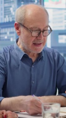 Vertical Video Senior çalışanları komisyoncuyla emeklilik sözleşmesi şartlarını okuyarak, gelecek için finansal yatırım sağlama seçeneklerini araştırıyorlar. Yaşlı çift uzmanla konuşuyor. Kamera A.