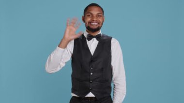 Otel müşterilerine gülümseyen ve el sallayan belboy çalışanı, insanları özgüvenle selamlıyor ve keyifli bir konaklama için lüks hizmetler sunuyor. Neşeli personel insanlara merhaba diyor. Kamera B.