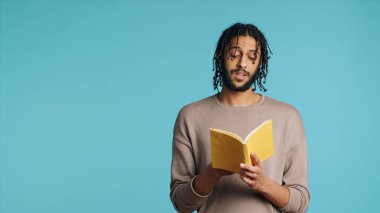 Middle Eastern man reading book from publisher aloud, telling story, enjoying hobby. BIPOC person narrating literature novel, doing critique essay, isolated over studio background, camera A clipart