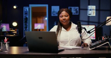 Afro-Amerikan kadın portresi canlı yayına profesyonel ekipman kullanarak başlıyor. İzleyicileri için içerik oluşturmaya hazır bir şekilde stüdyoya nüfuz eden kişi geliyor.