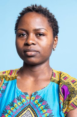 Çekici genç modelin portresi stüdyo arka planında poz veriyor, geleneksel renkli kıyafetler giyerken gülümsüyor. Afro-Amerikalı kadın kamerada şık etnik giysiler içinde kendini muhteşem hissediyor..