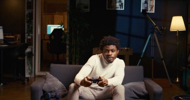 Adam ev sineması olarak kullanılan rahat oturma odasında TV 'de tek kişilik video oyunları oynamaya odaklanmış. Afrikalı Amerikalı oyuncu oyun konsolunda oyun oynamak için kumanda kullanıyor, kanepede dinleniyor.