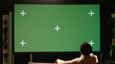 Adam yeşil ekran modern TV 'yi oturma odasında haber yayını yapmak için kullanıyor. VOD kanalını gösteren ultraviyole televizyon görüntülerini izleyen kişi kanepede dinleniyor.