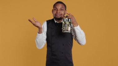 Garson, soslu bir şişe seti taşırken omuz silkiyor, kararsız davranıyor ve stüdyoda bir sembol göstermiyor. Profesyonel müşteri odaklı personel şaşkın ve emin değil. Kamera B.