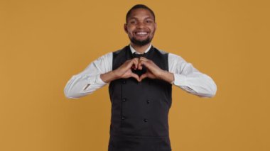 Önlüklü ve üniformalı garson stüdyoda kalp şeklinde bir işaret gösteriyor, samimi duygularını ve gerçek aşkını ifade ediyor. Yemek çalışanı romantik bir jest sunar kendine güveni tam tatlı adam. Kamera B.