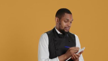 Önlüklü yetenekli garson müşterilerden yemek siparişlerini not defterine alır müşteri memnuniyeti için önemli bilgiler yazar. Hizmet odaklı sektörde çalışan kahya. Kamera A.