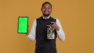 Sarı zemin üzerinde yeşil ekranlı tablet taşıyan erkek restoran çalışanları müşterilere servis yaparken kullanılan tuzluk ve biberlik setini taşıyorlar. Hizmet odaklı iş. Kamera B.