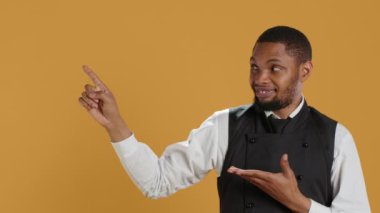 Profesyonel üniformalı garson, sağa ya da sola bir şey gösteriyor. Beş yıldızlı restoran reklamı yapıyor. Konukseverlik sektöründe yemek servisi. Kamera A.