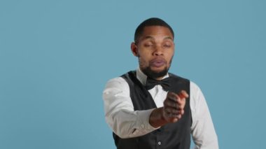 Otel hademesi beş yıldızlı pansiyonda misafirleri karşılıyor, gülümsüyor ve mavi arka planda insanları selamlıyor. Smokin ve kravat giyen bir işçi, turizm endüstrisi. Kamera A.