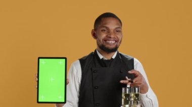 Sarı zemin üzerinde yeşil ekranlı tablet taşıyan erkek restoran çalışanları müşterilere servis yaparken kullanılan tuzluk ve biberlik setini taşıyorlar. Hizmet odaklı iş. Kamera A.