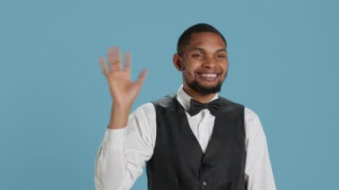 Otel müşterilerine gülümseyen ve el sallayan belboy çalışanı, insanları özgüvenle selamlıyor ve keyifli bir konaklama için lüks hizmetler sunuyor. Neşeli personel insanlara merhaba diyor. Kamera A.