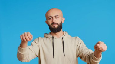Stüdyoda koro şefi gibi davranan genç bir müzisyen klasik gösteride bir grup için müzik yapıyor. Ortadoğulu bando şefi gibi davranıyor, mavi arka planda ciddi bir ifade var. Kamera 2.