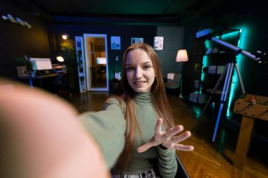 Gen Z gençlerinin POV 'u cep telefonuyla selfie çubuğunda giriş videosu kaydediyor, izleyicileri kanala üye olmaya davet ediyor. Stüdyodaki nüfuzlu kişi kendini çekmek için selfie makinesi kullanıyor.