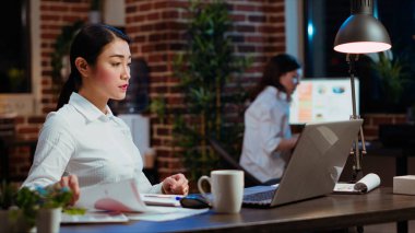 Bütün gece ofiste çalışan Asyalı muhasebeci mali veri grafiklerini ve grafiklerini kontrol etmekten sıkılmış. Sıkıcı evrak işlerini bitirmeye çalışan iş kadını. Stresli ve hafiflemiş hissediyor.